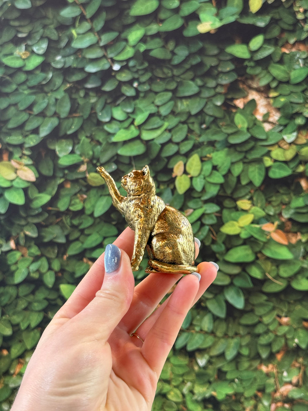 Brass gold cat figurine decor held by a hand against a green leafy background